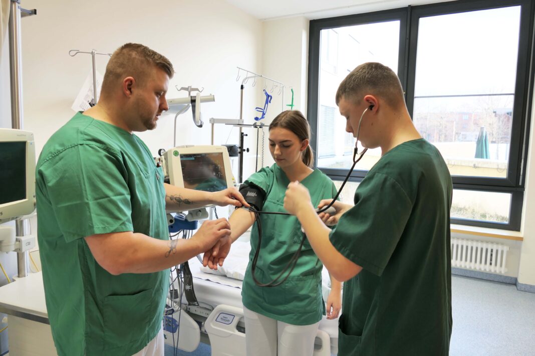 Der zentrale Praxisanleiter Philipp Teich (l.) zeigt Auszubildenden, wie man den Blutdruck misst. Foto: SKH Altscherbitz